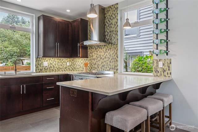 kitchen with pendant lighting, light countertops, stove, a sink, and wall chimney exhaust hood