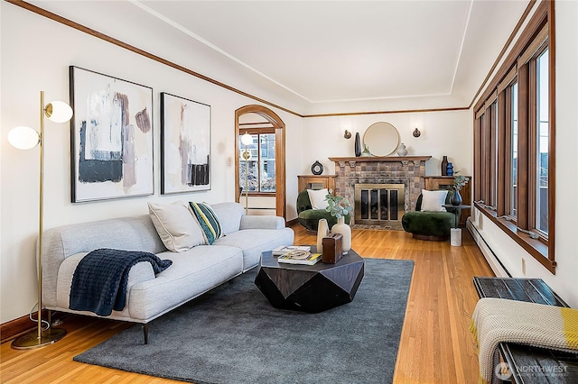 living area with crown molding, a fireplace, baseboard heating, and wood finished floors