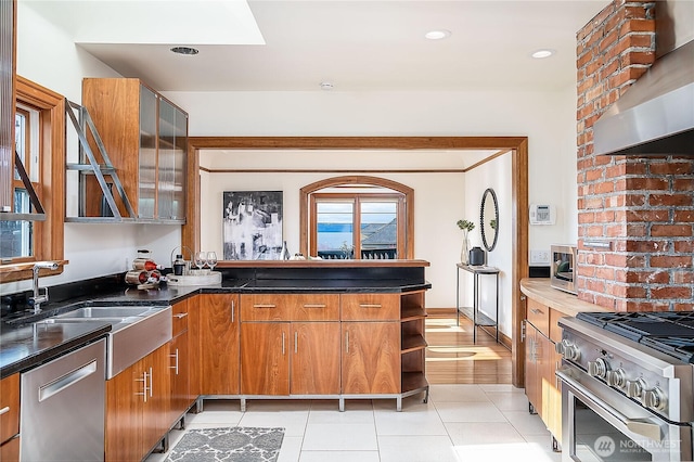 kitchen featuring a sink, appliances with stainless steel finishes, wall chimney exhaust hood, brown cabinets, and open shelves