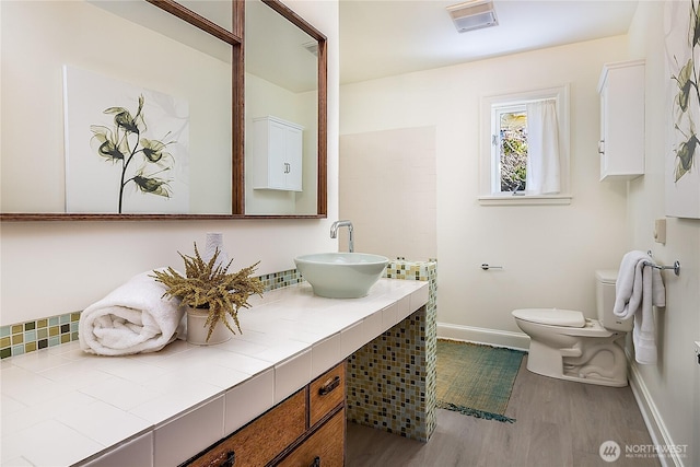 bathroom with toilet, wood finished floors, visible vents, vanity, and baseboards