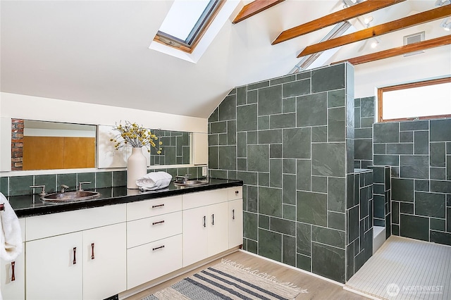 full bathroom featuring wood finished floors, a sink, tile walls, double vanity, and lofted ceiling with skylight