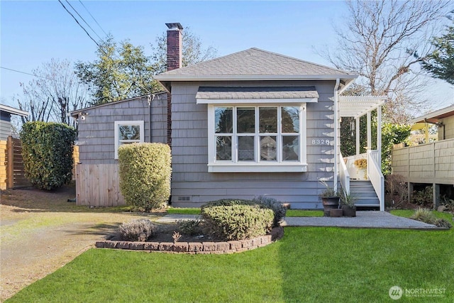 view of front of home with a chimney, a front yard, and roof with shingles