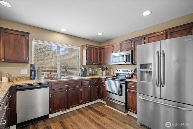 kitchen with light stone counters, appliances with stainless steel finishes, dark hardwood / wood-style flooring, and sink