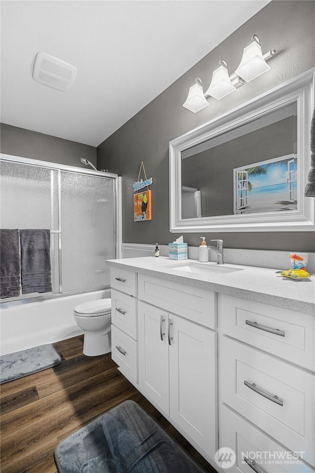 full bathroom featuring hardwood / wood-style flooring, vanity, combined bath / shower with glass door, and toilet