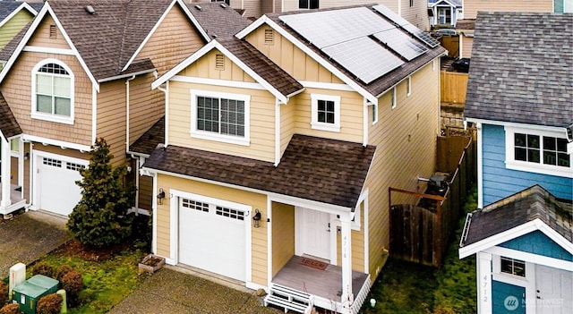 view of front of house with fence, roof with shingles, an attached garage, board and batten siding, and roof mounted solar panels