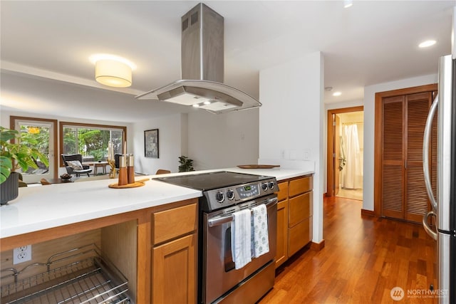 kitchen with light countertops, appliances with stainless steel finishes, brown cabinetry, light wood-style floors, and island range hood