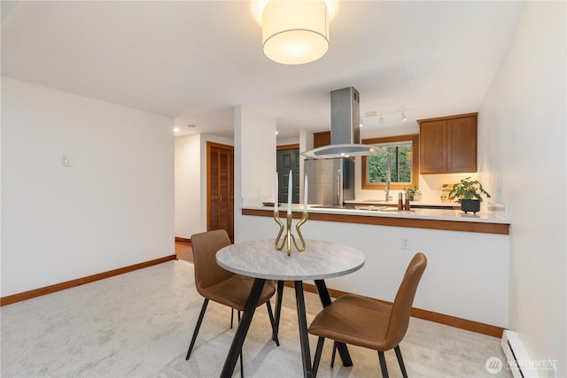 dining space with a baseboard radiator, rail lighting, light colored carpet, and baseboards