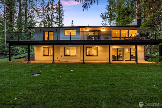 back house at dusk with a wooden deck and a lawn