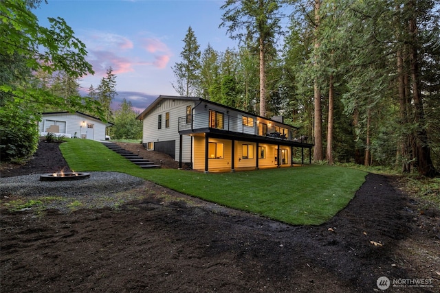 back house at dusk featuring a wooden deck, a lawn, and a fire pit