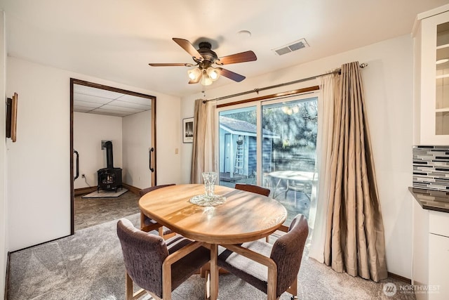 dining room with ceiling fan, carpet flooring, and a wood stove