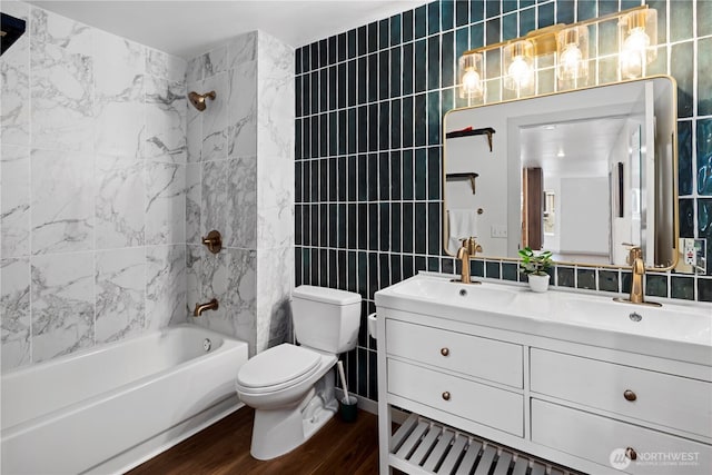 full bathroom with tile walls, vanity, wood-type flooring, tiled shower / bath, and toilet