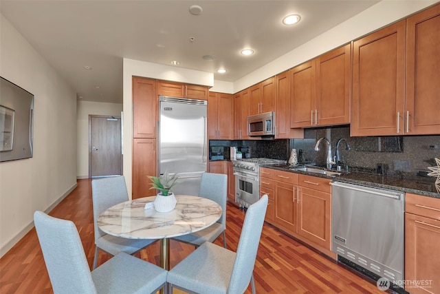 kitchen with high quality appliances, light hardwood / wood-style flooring, decorative backsplash, and dark stone countertops