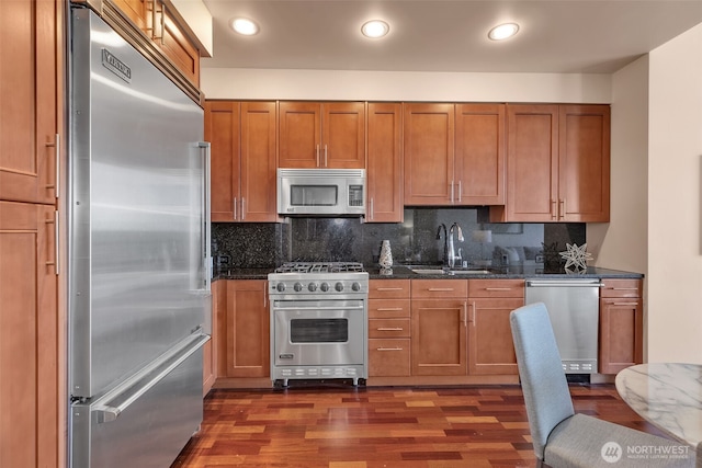 kitchen featuring dark wood-type flooring, sink, high end appliances, dark stone countertops, and backsplash