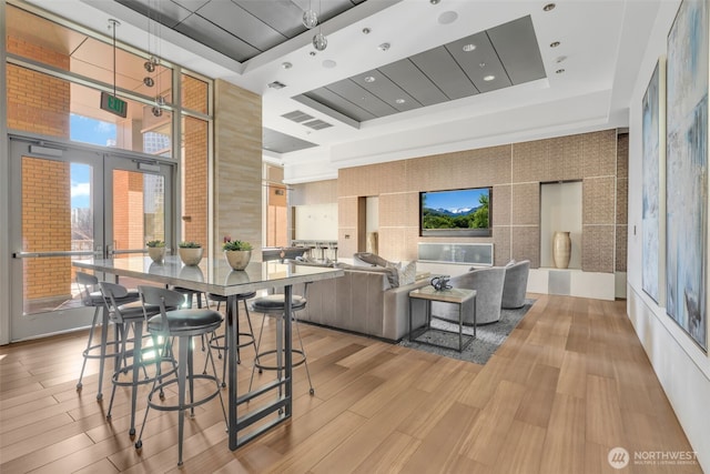 interior space with french doors, a towering ceiling, a raised ceiling, and light wood-type flooring