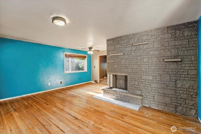 unfurnished living room with ceiling fan, a stone fireplace, and light wood-type flooring