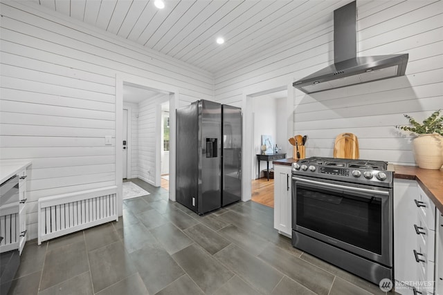 kitchen with appliances with stainless steel finishes, radiator heating unit, wall chimney range hood, wood counters, and white cabinetry