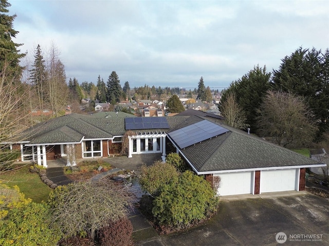 view of front of home featuring driveway, a shingled roof, an attached garage, and roof mounted solar panels