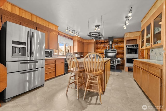 kitchen featuring a breakfast bar, light countertops, glass insert cabinets, appliances with stainless steel finishes, and a center island