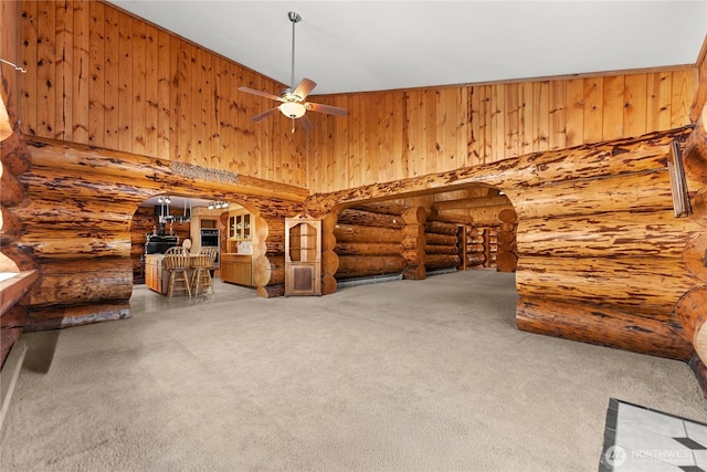 interior space with rustic walls, carpet flooring, a ceiling fan, and a towering ceiling