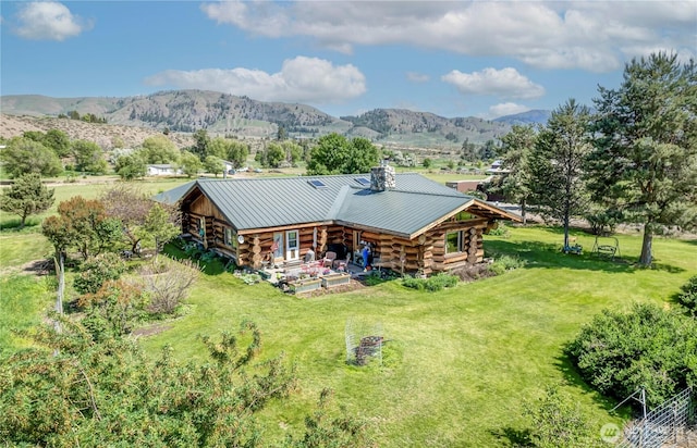 exterior space featuring a standing seam roof, a yard, log exterior, a mountain view, and metal roof