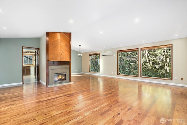 unfurnished living room featuring light hardwood / wood-style flooring, a notable chandelier, lofted ceiling, a wall mounted air conditioner, and a fireplace