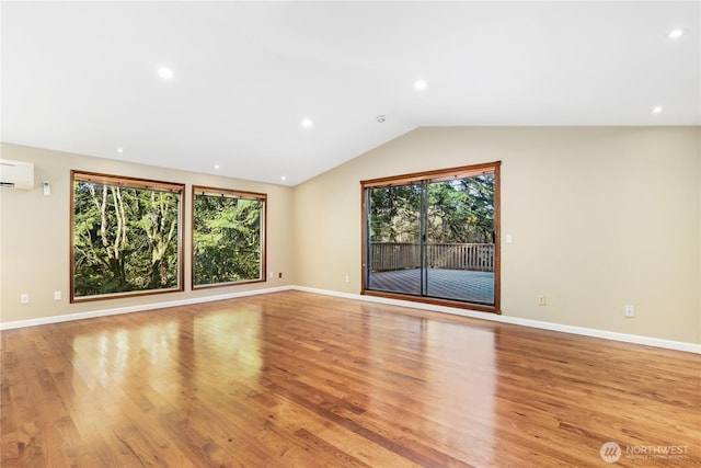 unfurnished living room featuring a healthy amount of sunlight, lofted ceiling, a wall mounted AC, and light hardwood / wood-style flooring