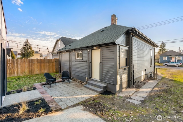 back of property with entry steps, a shingled roof, a chimney, fence, and a patio area