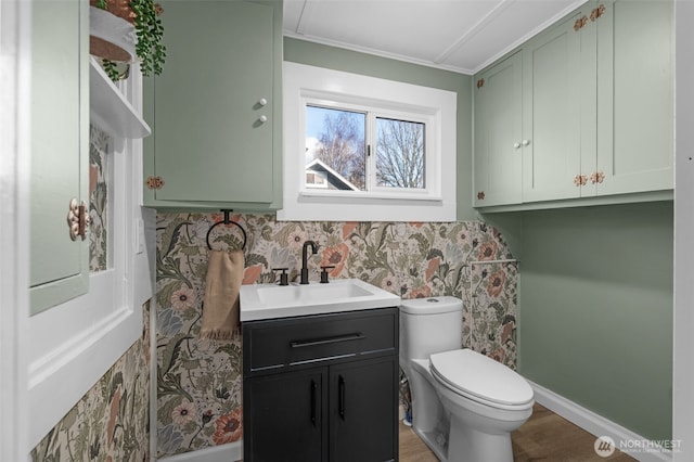 half bathroom with toilet, wood finished floors, vanity, baseboards, and crown molding