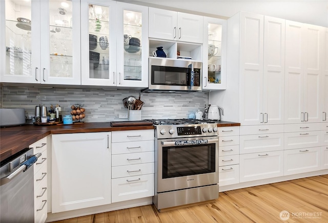 kitchen with appliances with stainless steel finishes, white cabinetry, wooden counters, decorative backsplash, and light wood-type flooring