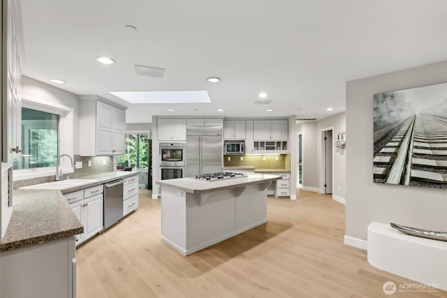 kitchen with white cabinetry, built in appliances, a skylight, a kitchen island, and light hardwood / wood-style floors