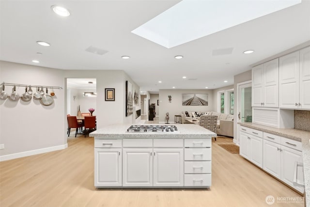 kitchen with light hardwood / wood-style flooring, white cabinetry, a skylight, tasteful backsplash, and stainless steel gas stovetop