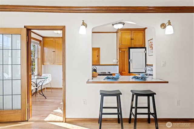 kitchen featuring a kitchen breakfast bar, backsplash, ornamental molding, light wood-type flooring, and kitchen peninsula