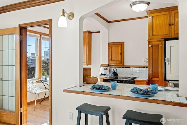 kitchen with light hardwood / wood-style flooring, tile counters, a breakfast bar area, ornamental molding, and tasteful backsplash