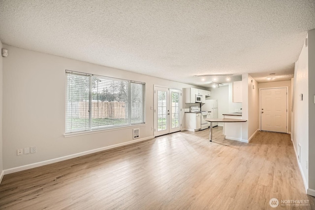 unfurnished living room featuring light wood finished floors, visible vents, baseboards, french doors, and a textured ceiling