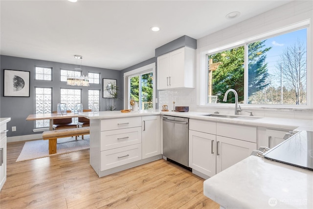 kitchen with sink, white cabinetry, decorative light fixtures, stainless steel dishwasher, and light wood-type flooring