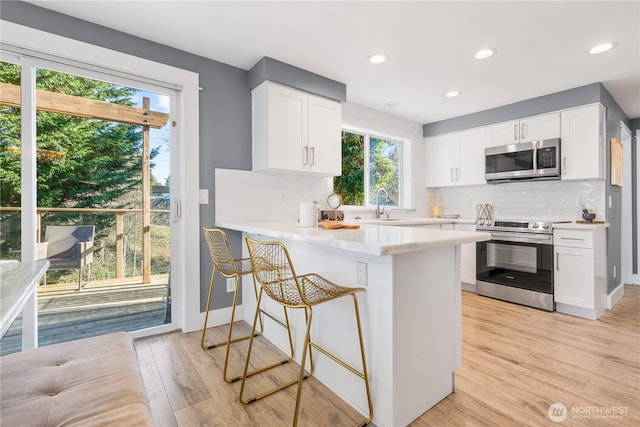 kitchen with appliances with stainless steel finishes, white cabinets, light wood-type flooring, and kitchen peninsula