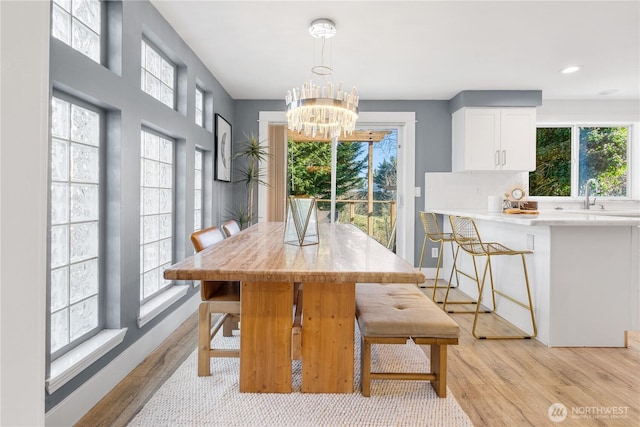 dining space featuring sink, a chandelier, a healthy amount of sunlight, and light wood-type flooring