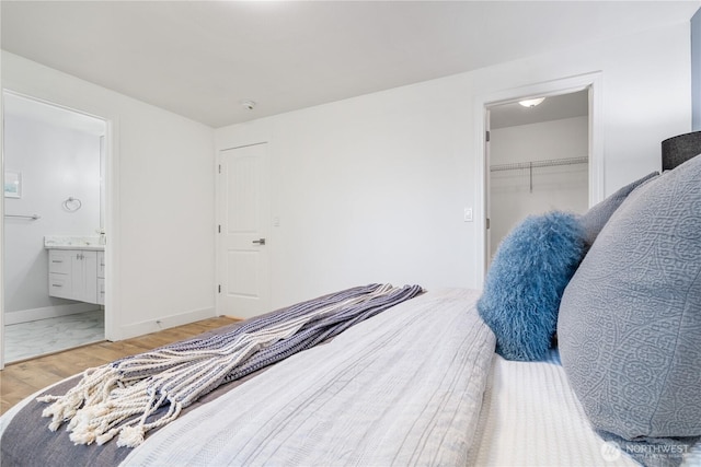 bedroom featuring ensuite bath, a spacious closet, a closet, and light wood-type flooring