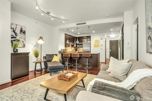 living room with dark hardwood / wood-style floors, wet bar, and track lighting