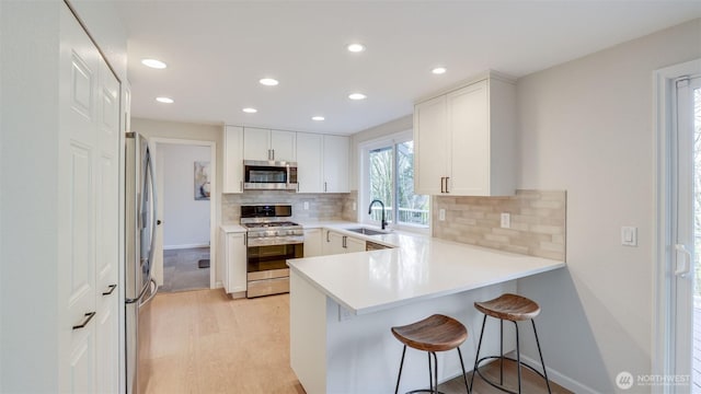 kitchen with light countertops, a peninsula, stainless steel appliances, light wood-style floors, and white cabinetry