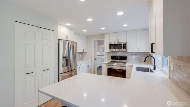 kitchen with a sink, backsplash, appliances with stainless steel finishes, a peninsula, and light countertops