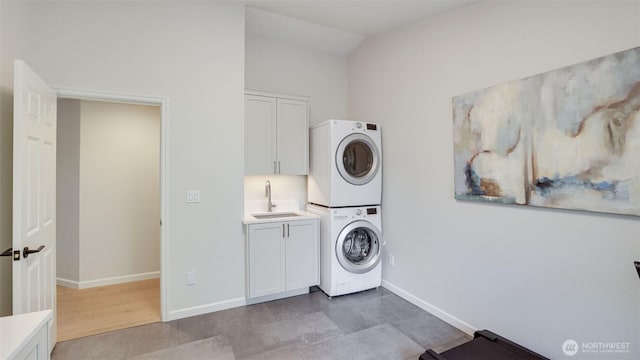 clothes washing area with a sink, baseboards, cabinet space, and stacked washing maching and dryer