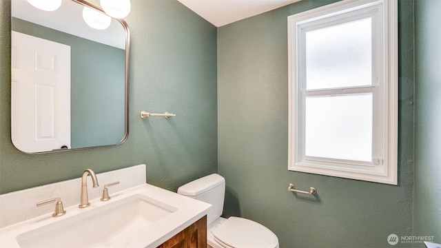 bathroom featuring toilet, vanity, and a textured wall