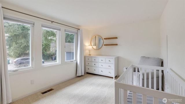 bedroom with a nursery area, visible vents, and light colored carpet