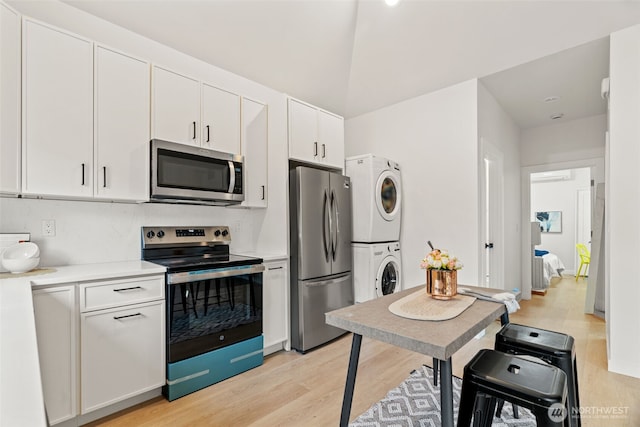 kitchen with stainless steel appliances, stacked washing maching and dryer, white cabinetry, and light hardwood / wood-style floors