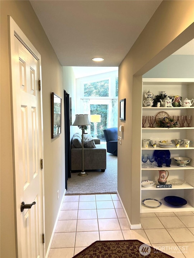 hallway with light carpet, light tile patterned floors, and baseboards