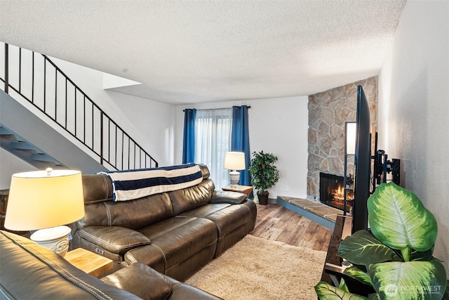 living room featuring hardwood / wood-style floors, a stone fireplace, and a textured ceiling