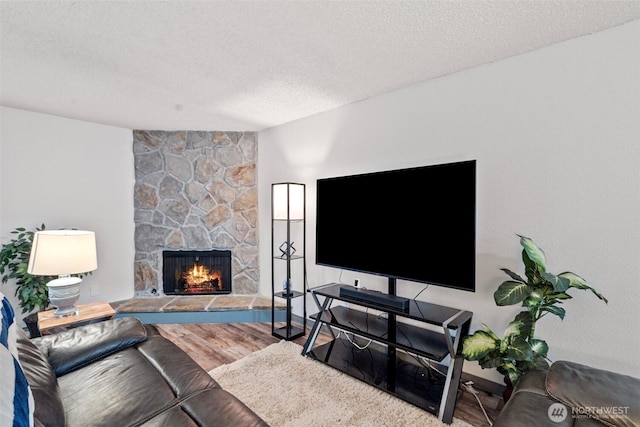 living room with a stone fireplace, a textured ceiling, and hardwood / wood-style flooring