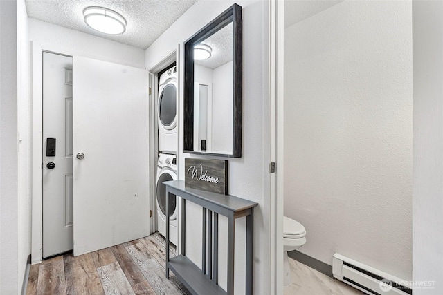 clothes washing area featuring hardwood / wood-style flooring, a baseboard radiator, stacked washing maching and dryer, and a textured ceiling