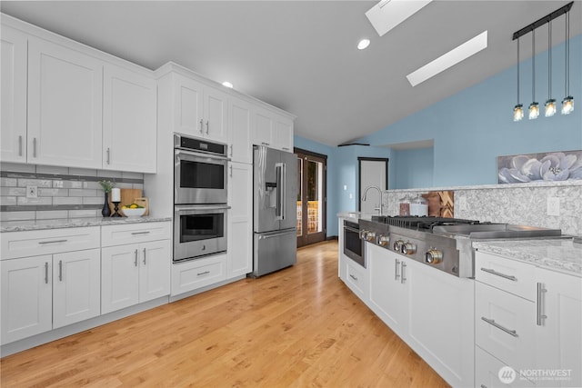 kitchen featuring white cabinetry, light wood-type flooring, pendant lighting, stainless steel appliances, and light stone countertops